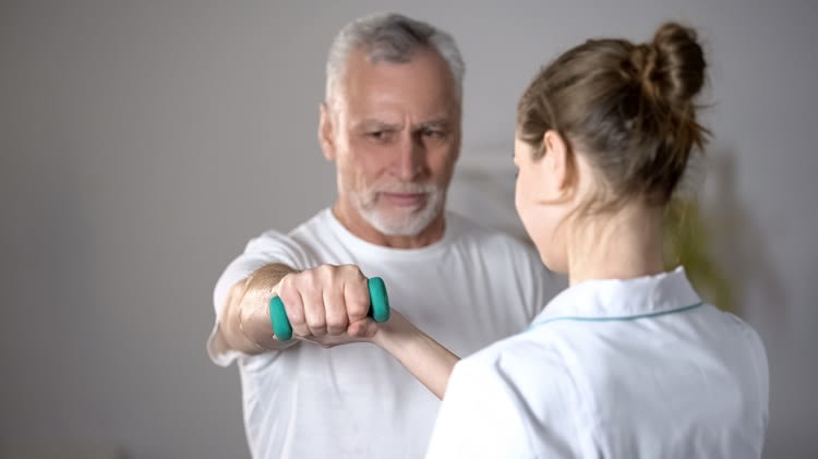 Médecin aidant un patient à effectuer des exercices de rééducation du bras avec des poids dans un cadre clinique.