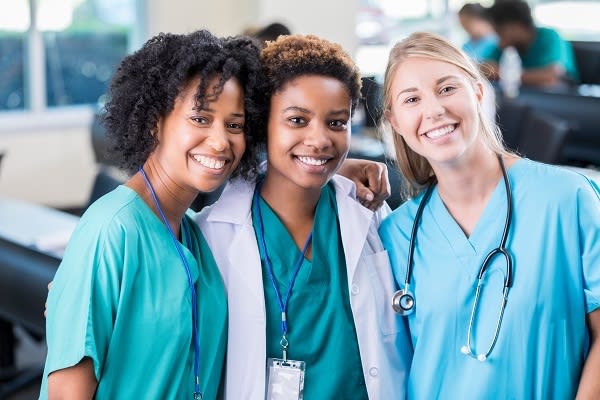three nurses wearing white coats and stethoscopes