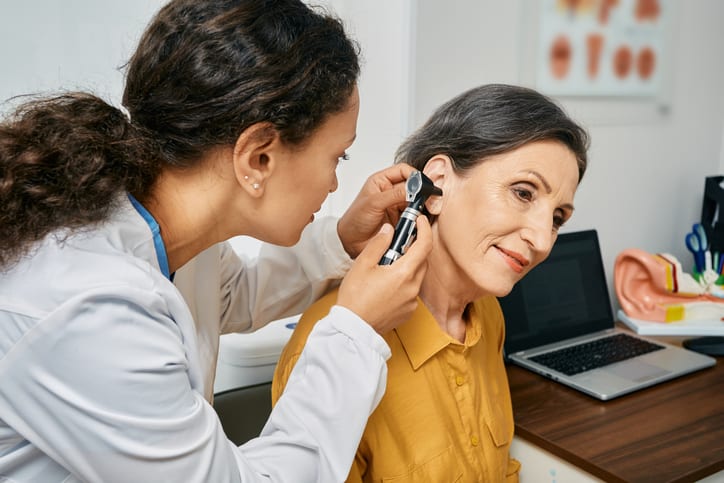 Doctor performing an ear examination using an otoscope on a patient in a clinical setting.