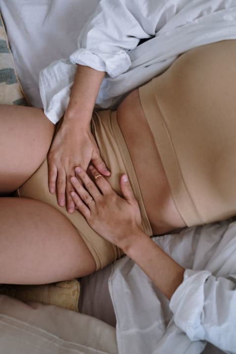 Photo montrant une personne allongée, les mains posées sur la région pelvienne et pubienne, illustrant la douleur et l’inconfort caractéristiques de la pubalgie.