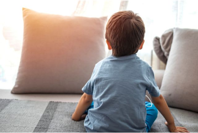 Autisme : enfant seul sur son lit de dos face à la fenêtre, entre deux coussins.