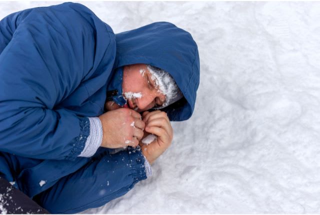 Hypothermie. Image d'un homme emmitouflé dans une doudoune bleu, allongé inconscient sur la neige.