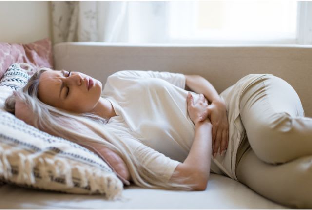Dysménorrhée. Image d'une femme allongée sun un divan et qui tient son ventre de douleur.