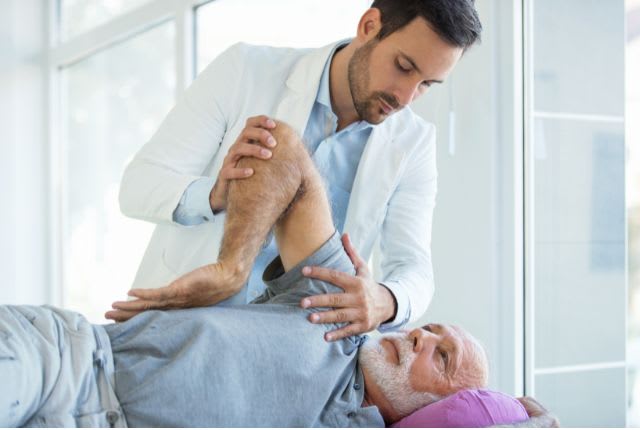 Capsulite : un soignant examine l'épaule et le bras d'un patient âgé allongé.