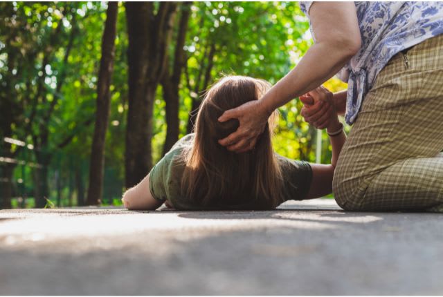Crise d'épilepsie : une personne vient au secours d'une femme allongée par terre.