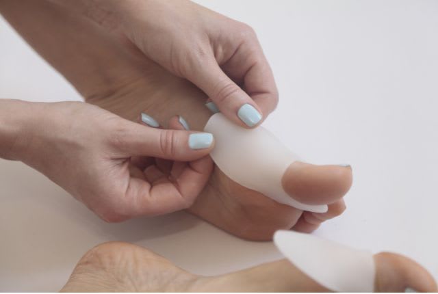 Image de mains de femme en train de poser une orthèse sur son gros orteil.