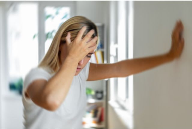 Méningite. Image d'une femme se tenant la tête de douleur, yeux fermés, prenant appui sur un mur.
