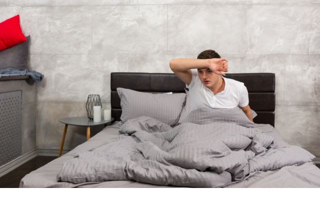 Sueurs nocturnes. Un homme s'éponge le front dans son lit.