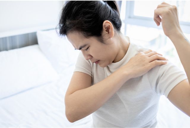 Tendinite de l'épaule : une femme assise sur un lit se masse l'épaule.