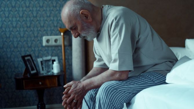 Quels sont les premiers symptômes du cancer de la prostate ? Image d'un homme âgé assis sur le bord de son lit.