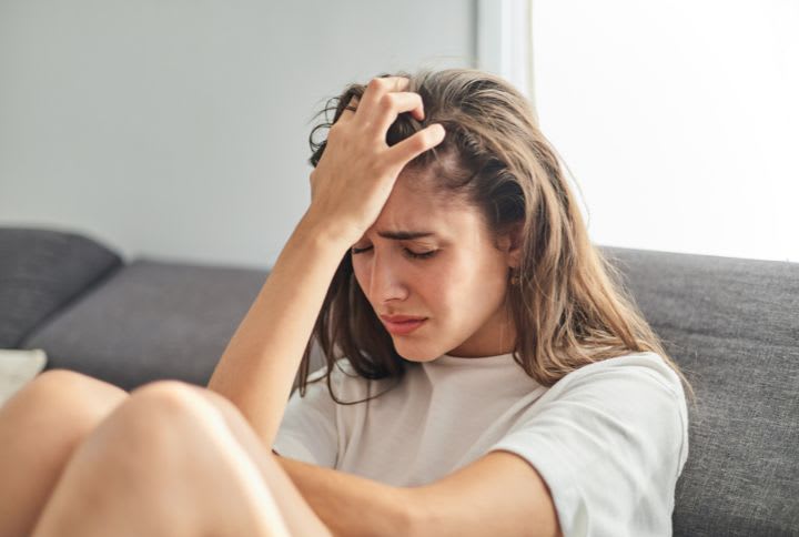 Anxiété estivale : image d'une jeune fille assise sur un canapé, en proie à un épisode d'anxiété estivale