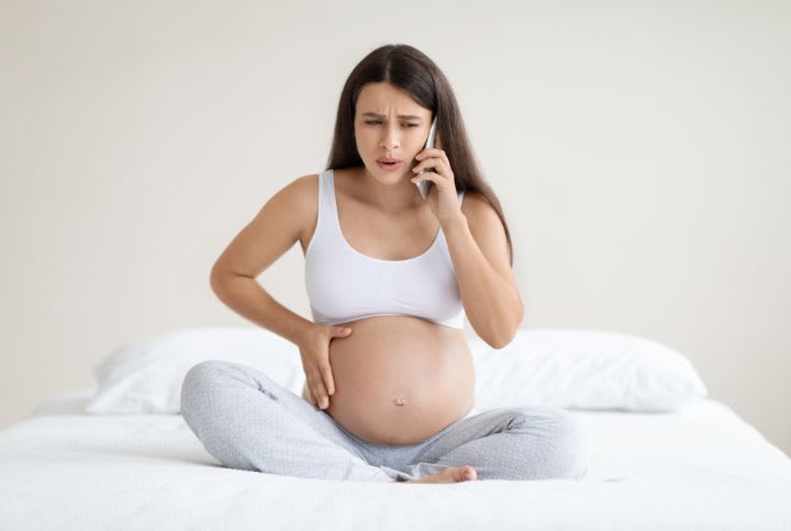 Contraction de Braxton : image d'une femme enceinte assise en tailleur souffrant de contractions de Braxton