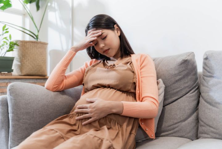 Maux de tete grossesse : image d'une femme enceinte assise sur un canape, qui souffre de maux de tete