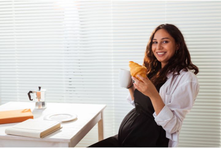 Congé maternité : une jeune femme enceinte prend son petit déjeuner.