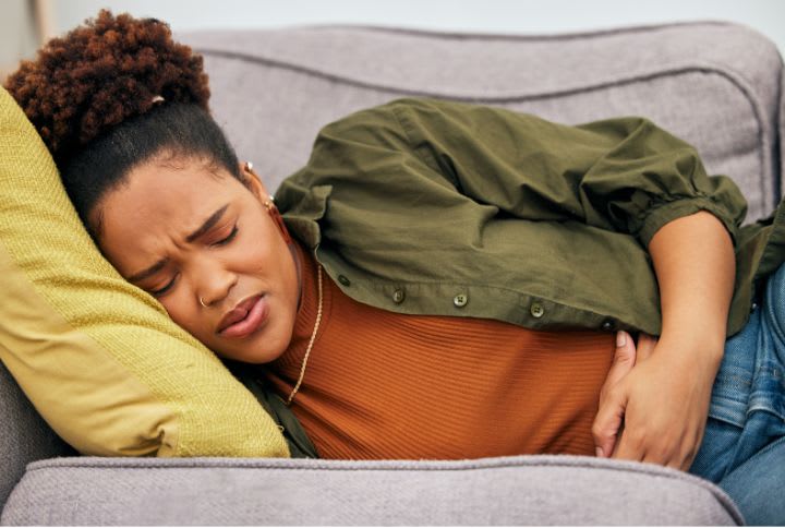 Nausee et vomissement durant la grossesse : une femme allongée la tête sur un coussin, visiblement mal à l'aise, yeux fermés, soufflant par la bouche et se tenant le bas du ventre.