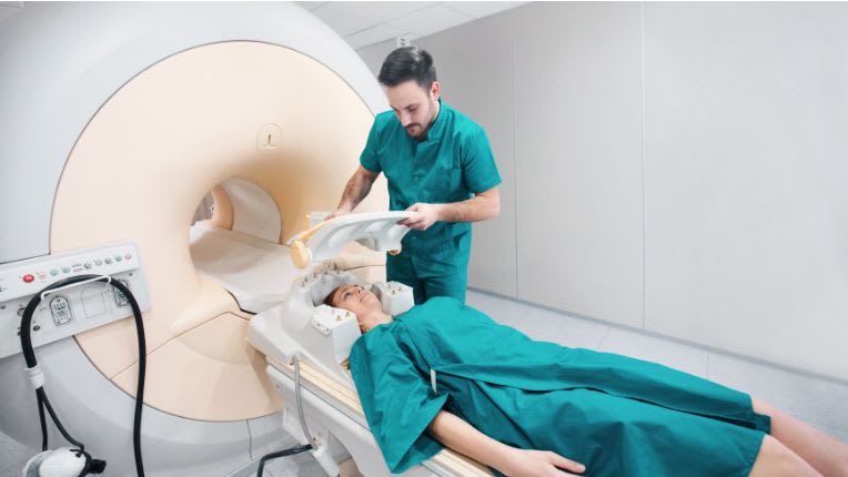 IRM - Matériel et équipement de radiologie : image d'une IRM avec son tunnel. Un soignant aide une patiente à s'installer.