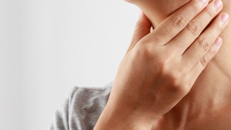 Gros plan sur une femme qui se tient la gorge de douleur.