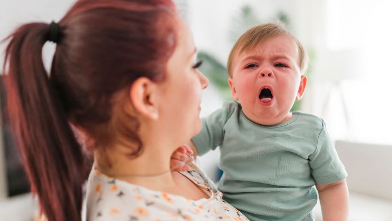 Bronchiolite : définition, causes et traitements. Une maman porte une bébé qui tousse et dont le visage est tout rouge.