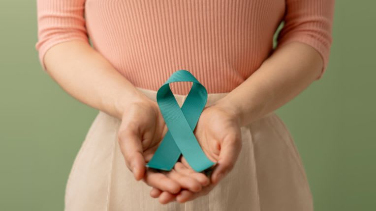 Cancer du col de l’utérus : prévention, dépistage, vaccination en 2025. Une femme dont on voit le torse et le haut des jambes présente un ruban bleu contre les cancers gynécologiques.