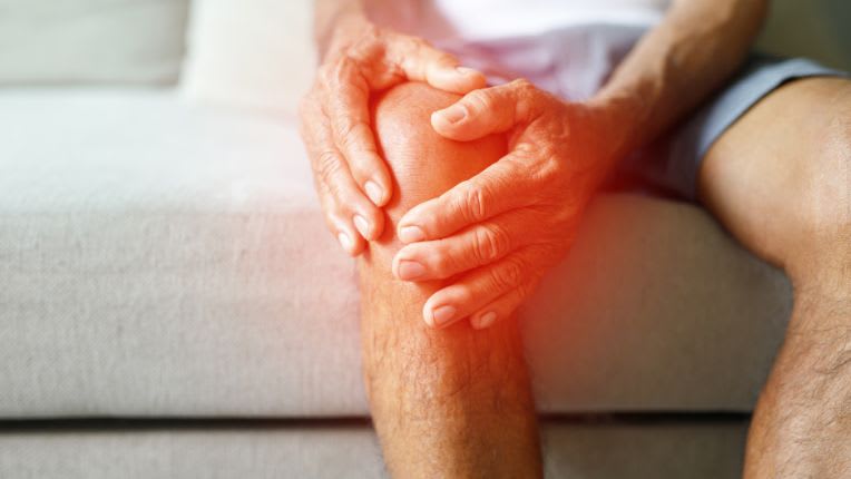 Diclofénac (Voltarène) : indication, rhumatismes, posologie, conseils. Image centrée sur un genou qu'une personne entoure de ses mains. Un halo de lumière rouge souligne qu'il est douloureux.