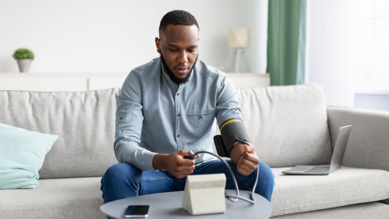 Journée mondiale de l'hypertension 2025 : un jeune homme assis sur un canapé prend sa tension.