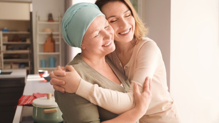 Journée mondiale contre le cancer 2026 : dépistage, prévention et enjeux. Deux femmes sont enlacées, dont une porte un bonnet bleu sur la tête.