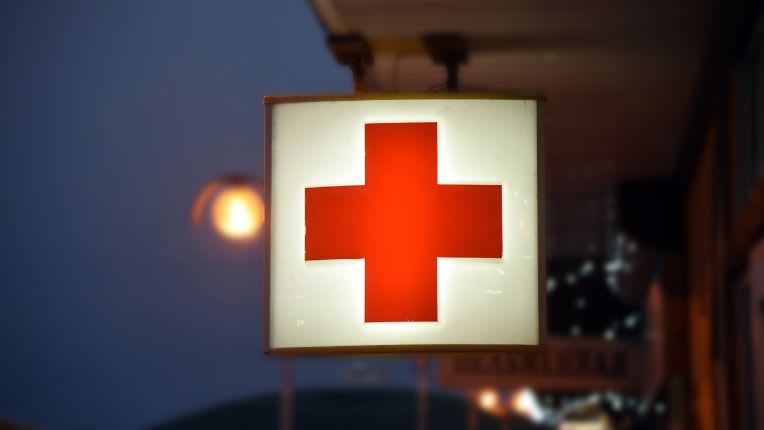 Méningites bactériennes à méningocoques. Image d'une enseigne lumineuse portant une croix rouge, marquant l'emplacement des urgences.