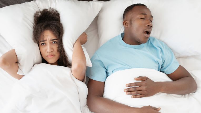 Polygraphie. Couple au lit, l'homme ronfle et sa femme se bouche les oreilles. L'apnée du sommeil peut être diagnostiquée grâce à l'examen de polygraphie respiratoire.
