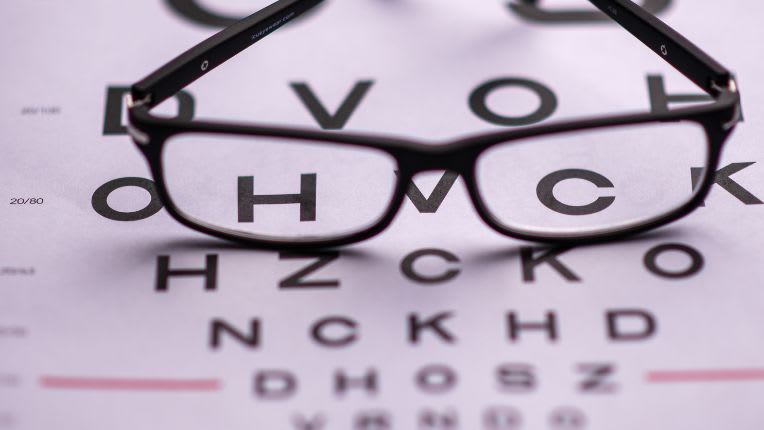 Presbytie. Image montrant un tableau de lettres dont les plus petites sont floues, avec une paire de lunettes noires posée dessus.