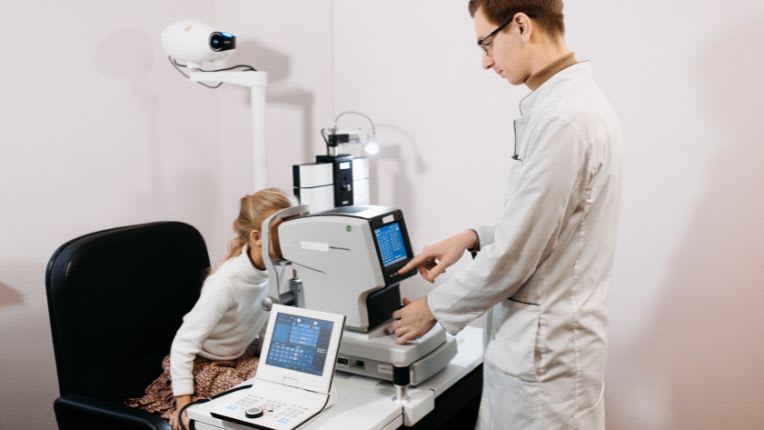 Rétinoblastome. Une petite fille regarde dans un appareil d'ophtalmologie manipulé par un soignant.