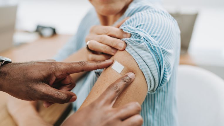rdv vaccin fievre jaune. Photo d'un bras avec manche relevée, sur lequel un soignant applique un pansement après une vaccination.