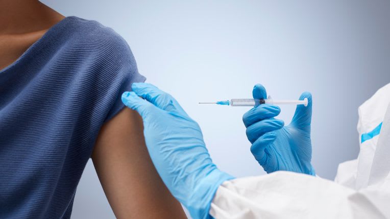 rdv vaccin fievre jaune. Image d'une seringue tenue par un soignant en gant bleu qu'il dirige vers le bras d'une de ses patientes.