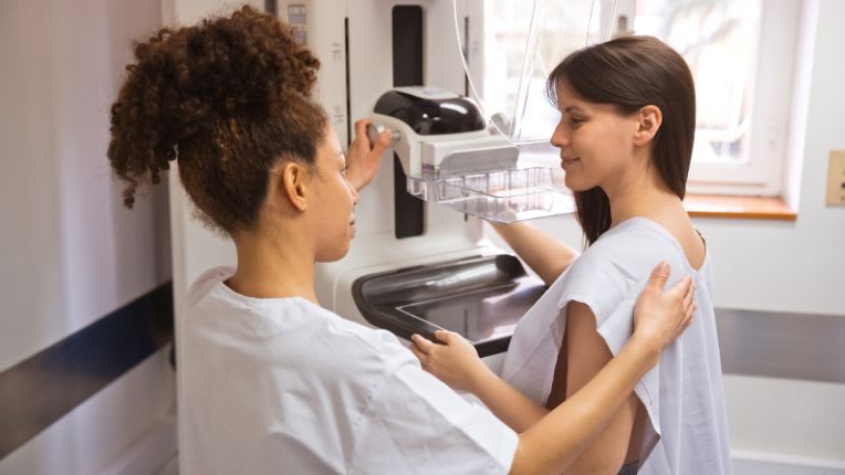 Mammographie. Est-elle douloureuse ? Une soignante installe et discute avec une patiente devant un appareil de radiologie.