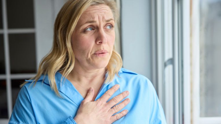 Palpitations. Une femme porte sa main à son cœur et souffle.