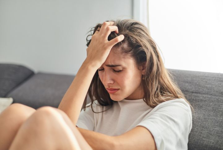 Anxiété estivale : image d'une jeune fille assise sur un canapé, en proie à un épisode d'anxiété estivale