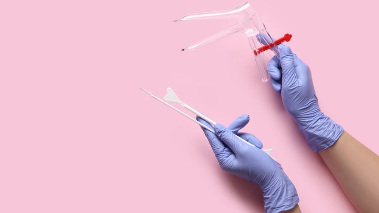 Santé des femmes. Dépistage du cancer du col de l'utérus. Sous un fond rose, des mains gantées de soignant présentent les instruments qui servent à réaliser un frottis : speculum et kit de test Pap.