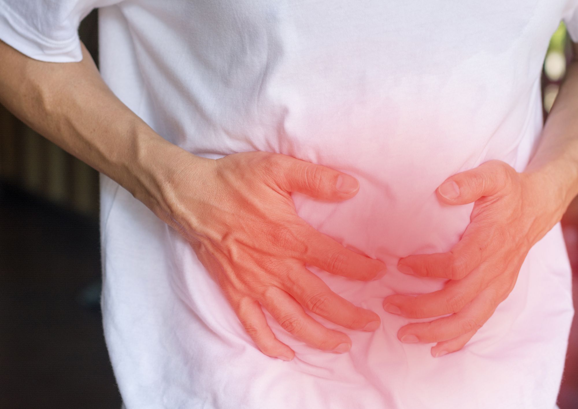 homme avec un teeshirt blanc qui tient son ventre comme de douleur, avec un espace en rouge sur le ventre pour montrer la douleur 