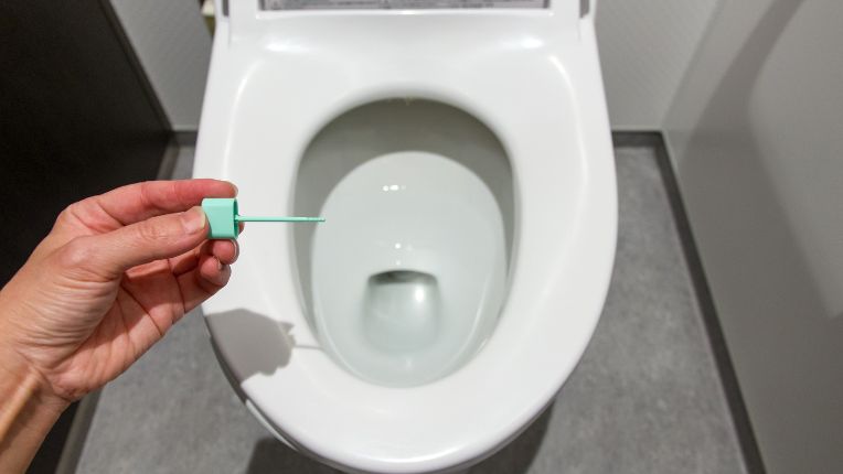 Est-ce que le dépistage du cancer du côlon marche ? Image d'une main qui montre une tige de prélèvement du kit de dépistage du cancer colorectal, au-dessus des wc.