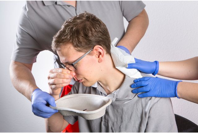 épistaxis : deux personnes tiennent un jeu au dessus d'une cuvette alors qu'il saigne du nez.