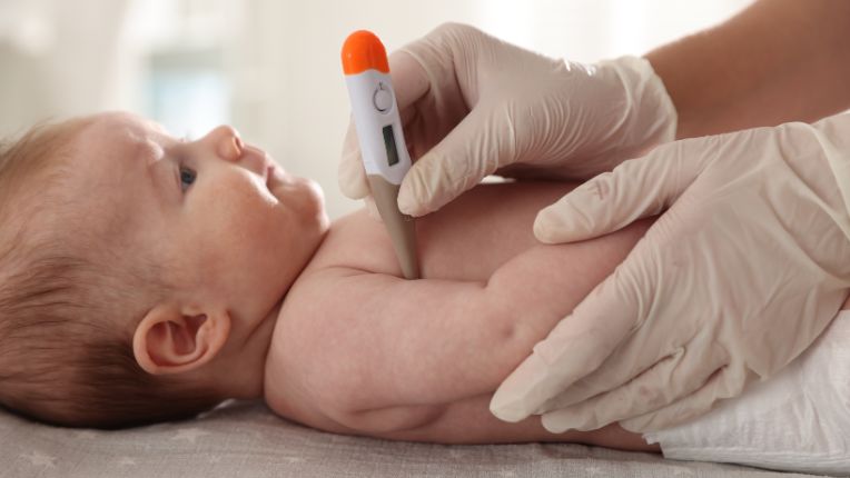 L’essentiel sur la bronchiolite, l’épidémie 2025 et les moyens de se protéger. Image d'un nourrisson allongé avec la main d'un soignant en train de prendre sa température sous le bras.