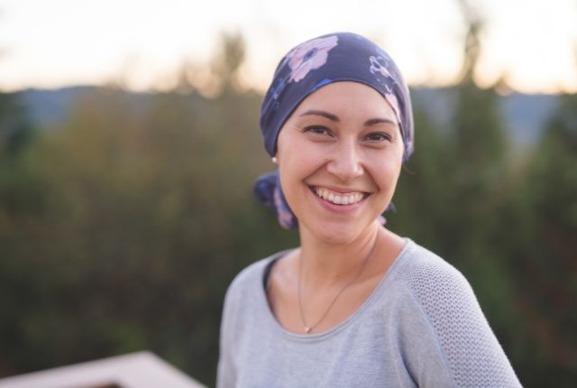 Cancer chez les jeunes. Une jeune femme souriante porte un foulard sur la tête pour masquer la perte des cheveux liée aux traitements anticancéreux.