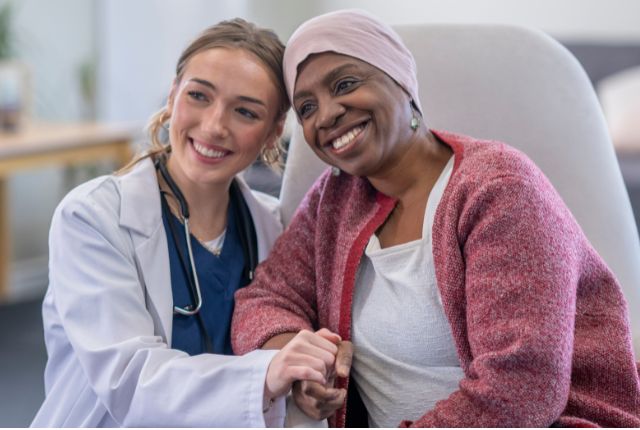 Cancer féminin. Une patiente avec un foulard sur la tête et une soignante sourient et se tiennent la main.