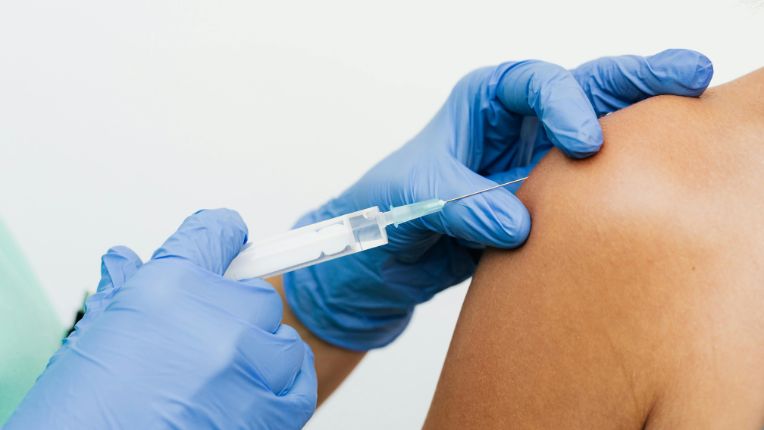 Centre de vaccination Internationale Lyon Parc. Vaccin contre le chikungunya. Image des mains d'un soignant avec des gants bleus en train d'injecter un vaccin dans l'épaule d'une personne.