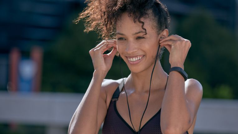 Dopamine : les secrets de ce neurotransmetteur du plaisir. Photo d'une jeune femme, en tenue de sport, souriant de bien-être en écoutant de la musique.