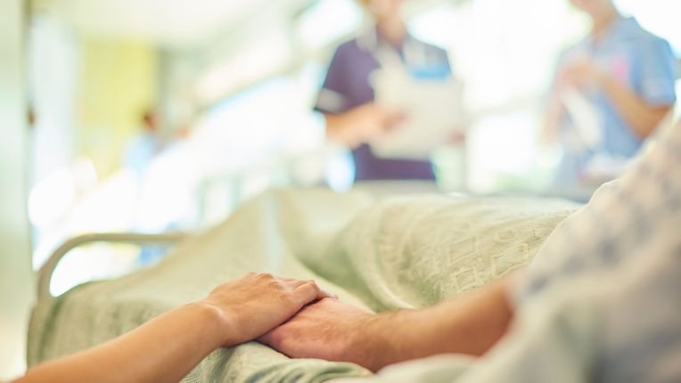 Une épidémie de grippe toujours intense et mortelle en janvier 2025. Une femme tient la main d'une personne âgée allongée sur un lit d'hôpital, avec des soignants à son chevet.