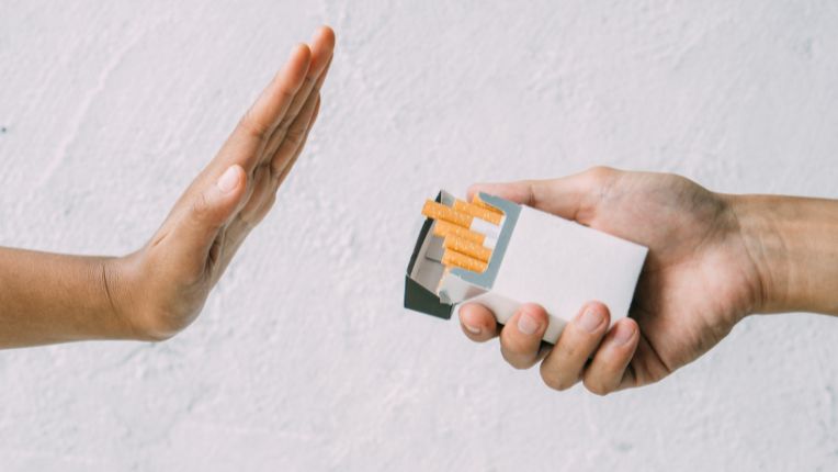 Journée mondiale sans tabac 2025 : photo en gros plan sur une main à droite qui tient un paquet et propose une cigarette à une main à gauche levée en signe de refus.