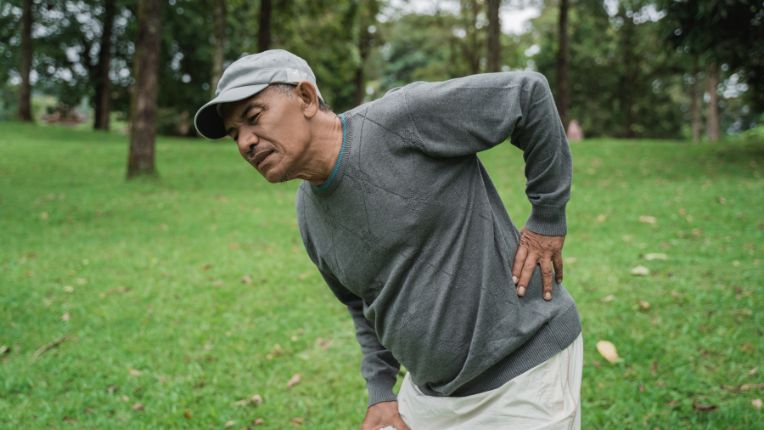 Lumbago — définition, causes et traitements. Elsan. L'image montre un homme d'âge moyen penché et se tenant la taille de douleur.
