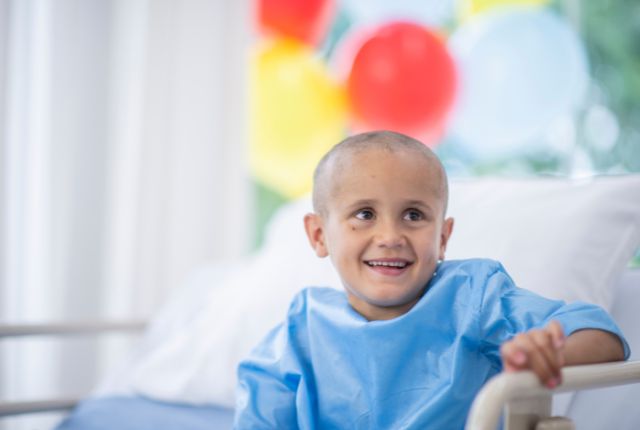 Médulloblastome : définition, symptômes, espérance de vie. Image d'un jeune enfant souriant portant une blouse bleue sur son lit d'hôpital.