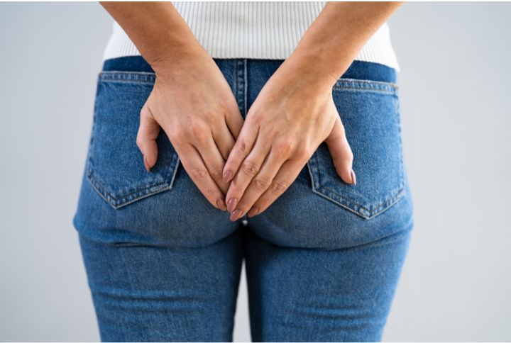 Mycose anale et démangeaisons (prurit) : une femme habillée d'une paire de jean's, vue de dos, pose ses mains sur ses fesses.
