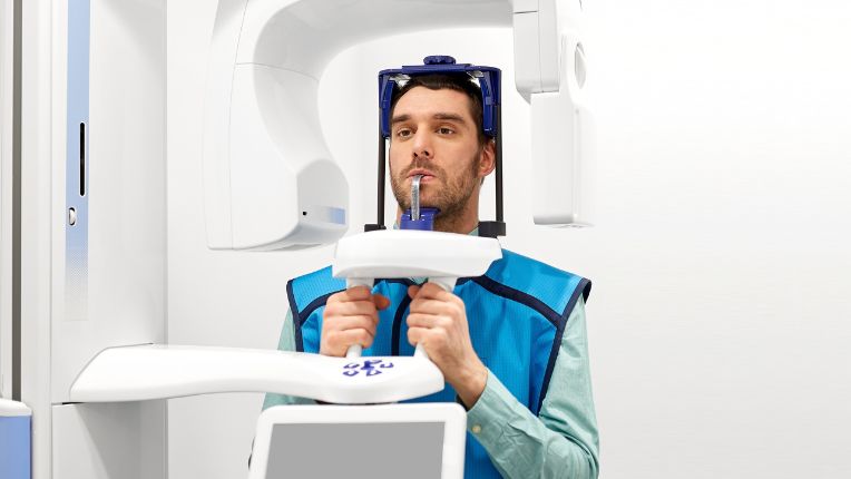 Quelle est la différence entre une radio et un scanner ? Patient avec le visage posé sur un instrument de radiologie dans un cabinet dentaire.